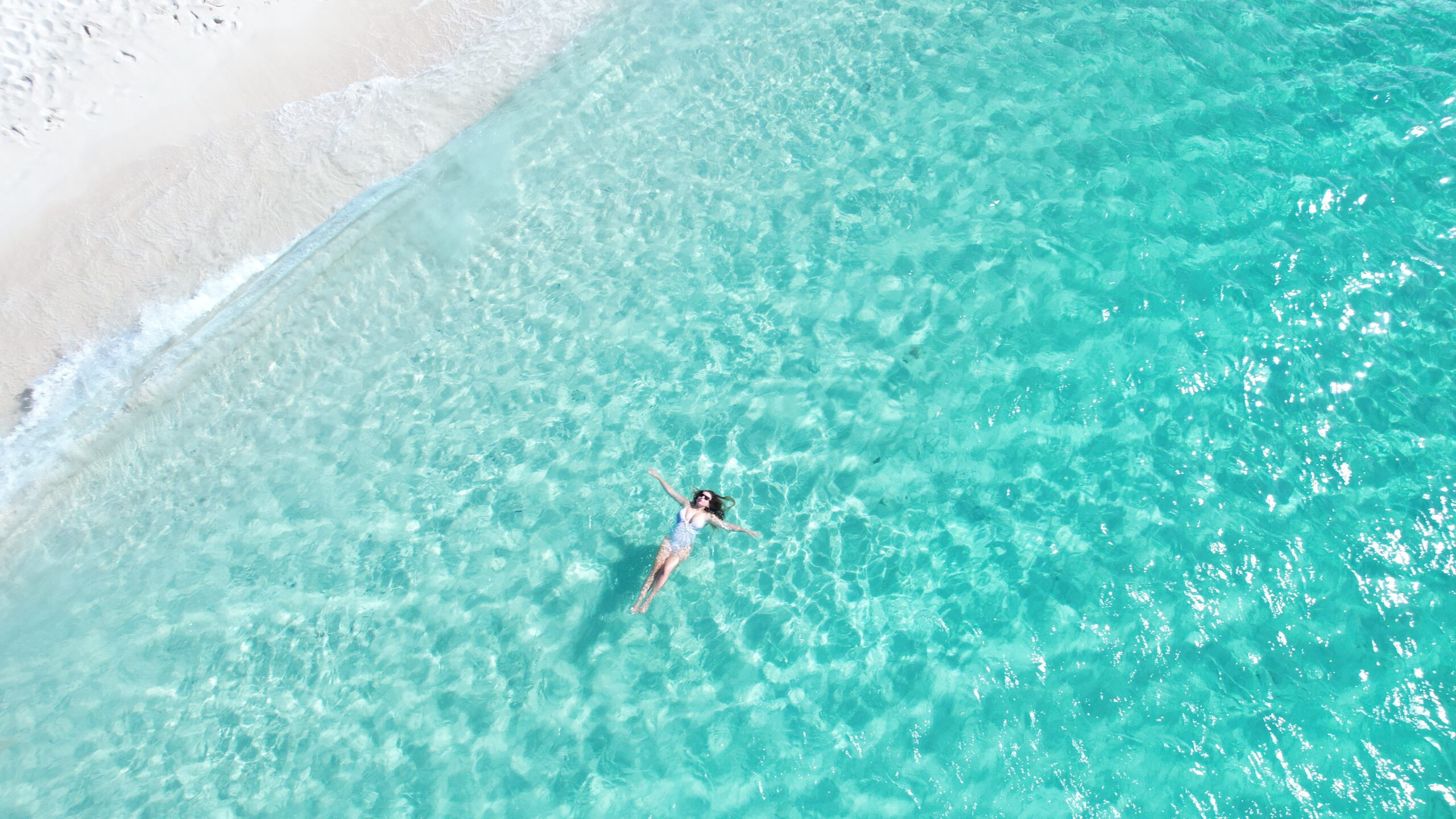Guest floating in shallow turquoise water near a beach in Turks and Caicos